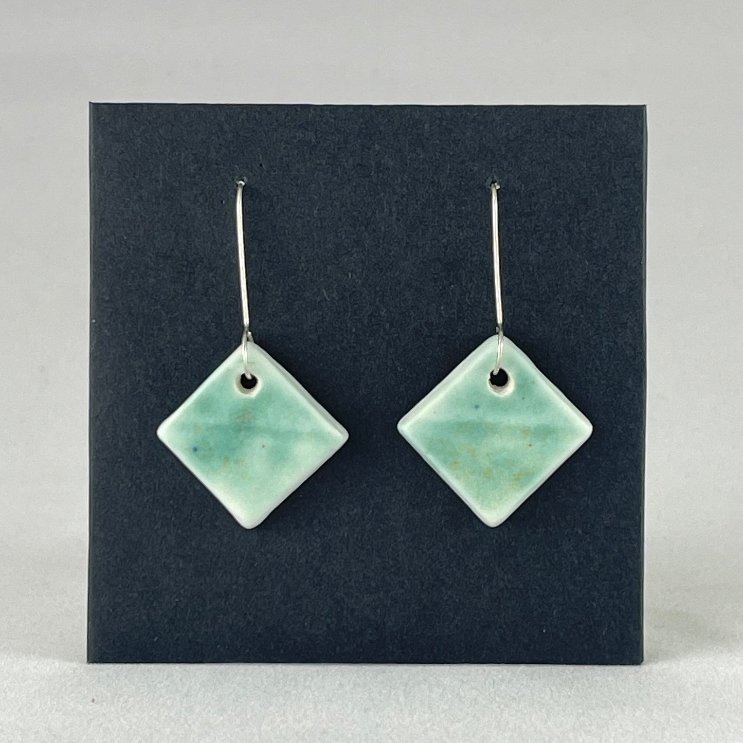 A pair of diamond shaped porcelain earrings in green. On sterling silver earrings hooks.