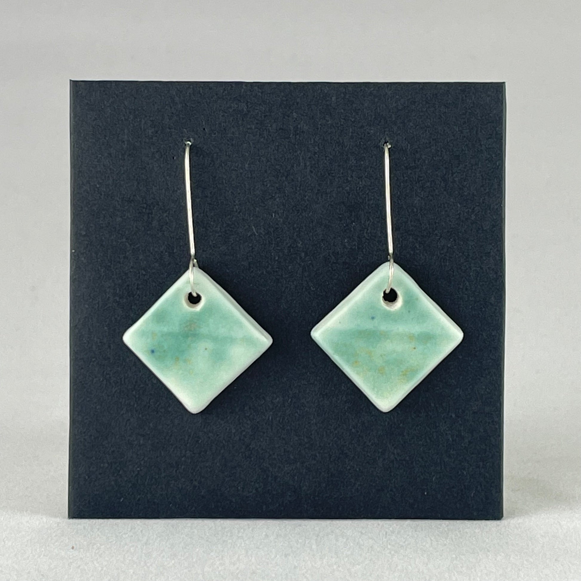 A pair of diamond shaped porcelain earrings in green. On sterling silver earrings hooks.