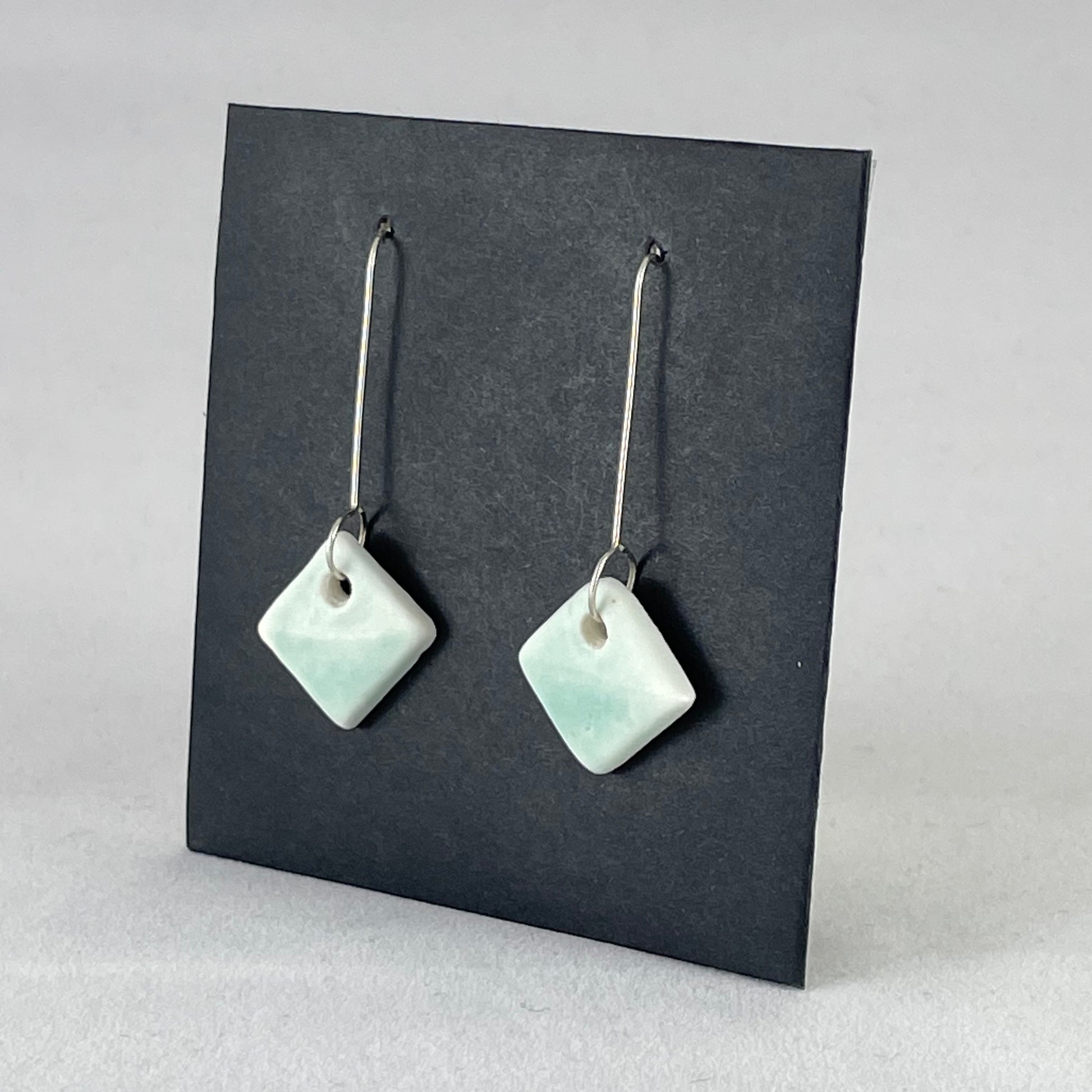 A pair of diamond shaped porcelain earrings in green. On sterling silver earrings hooks. Side view
