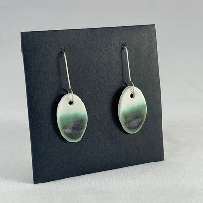 Pair of emerald green and white oval shaped porcelain earrings. Top half white and bottom half textured green. Sterling silver hooks. Side view
