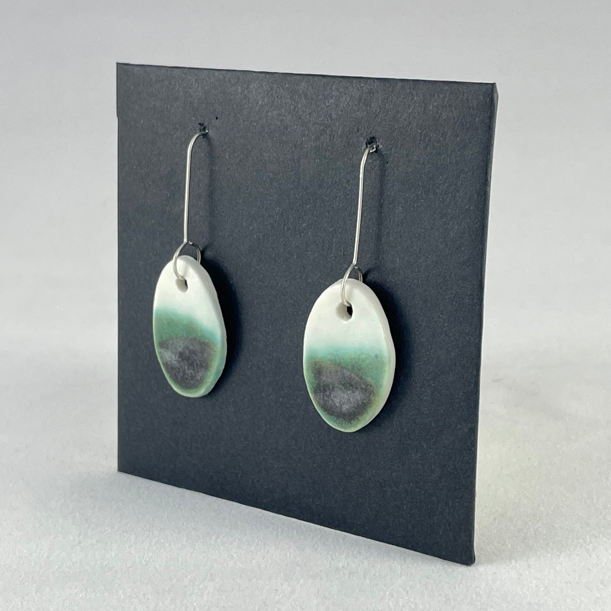 Pair of emerald green and white oval shaped porcelain earrings. Top half white and bottom half textured green. Sterling silver hooks. Alternate side view 
