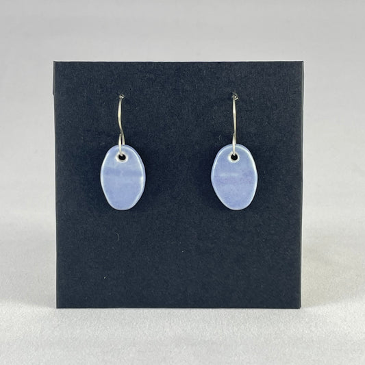 A pair of oval shaped porcelain earrings in blue. Photographed on a black background. On sterling silver earrings hooks.