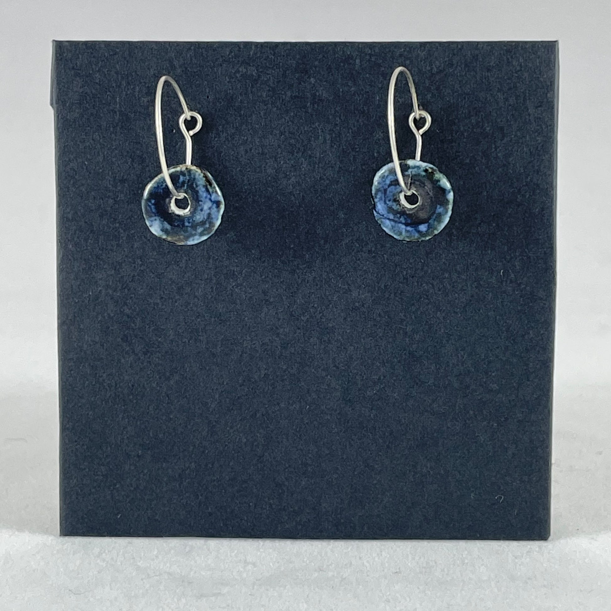 A pair of blue hand coiled porcelain earrings on sterling silver hoops. Photographed on a graphite coloured background