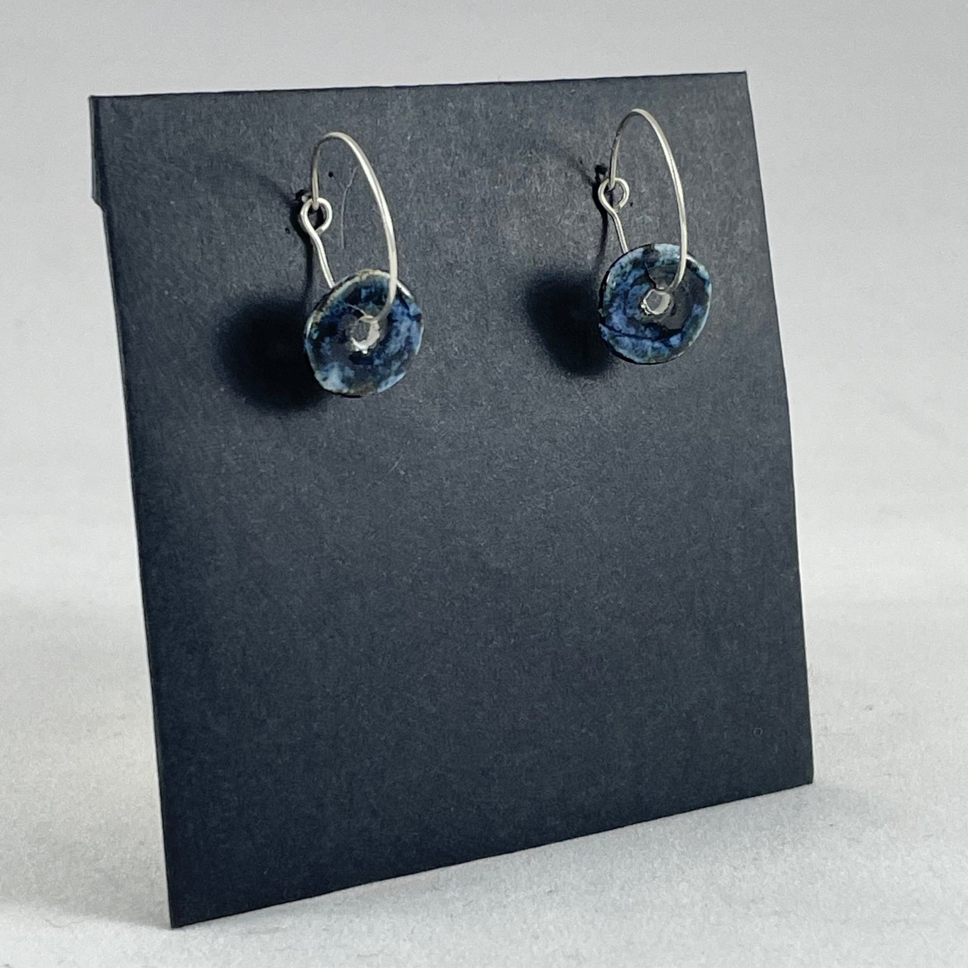 A pair of blue hand coiled porcelain earrings on sterling silver hoops. Photographed on a graphite coloured background. Closeup of one earring