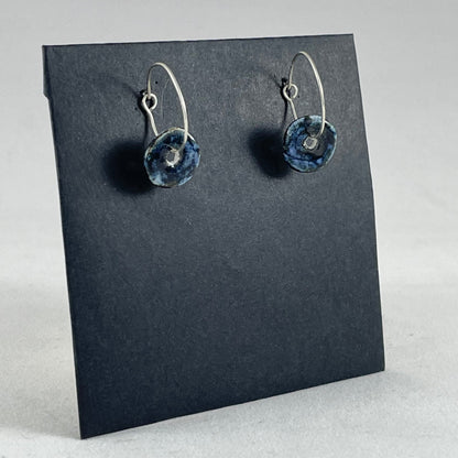 A pair of blue hand coiled porcelain earrings on sterling silver hoops. Photographed on a graphite coloured background. Closeup of one earring