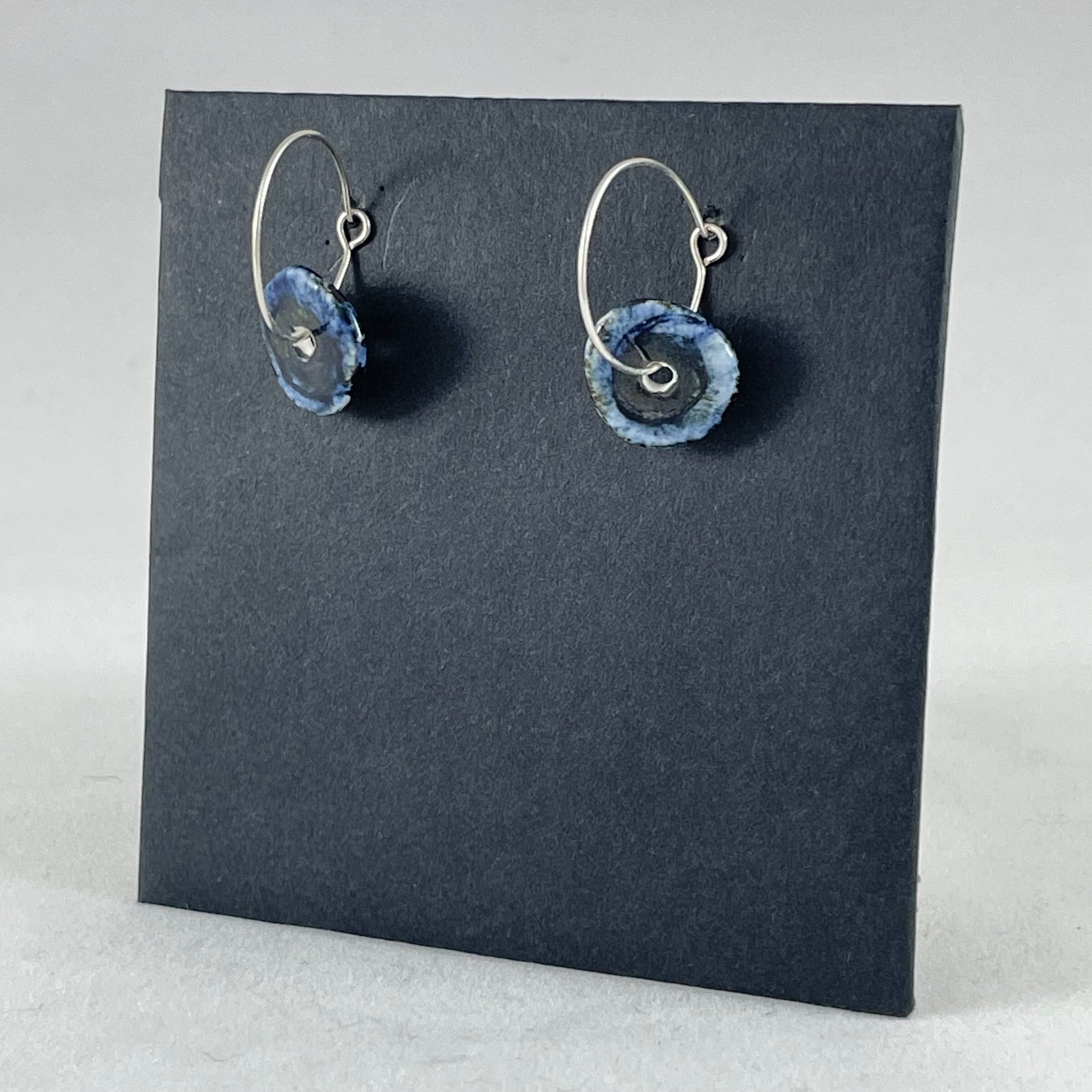 A pair of blue hand coiled porcelain earrings on sterling silver hoops. Side view