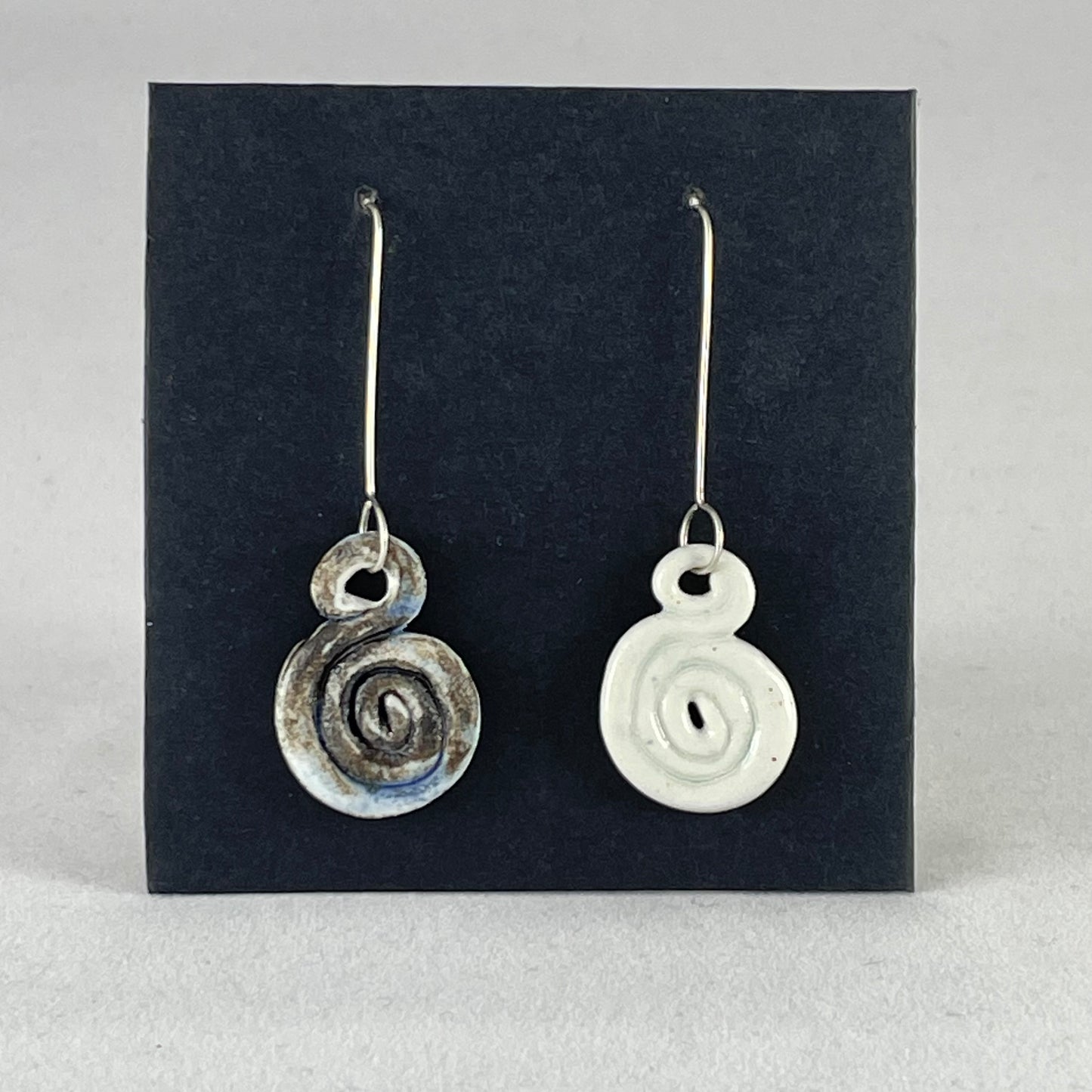 A pair of hand coiled porcelain earrings. One earring is white and the other is blue and black. Photographed on a black background. On sterling silver earrings hooks. 