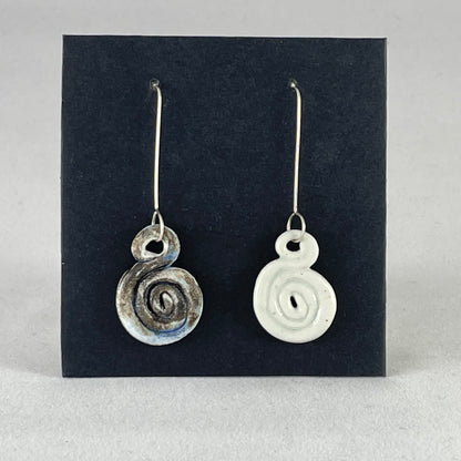 A pair of hand coiled porcelain earrings. One earring is white and the other is blue and black. Photographed on a black background. On sterling silver earrings hooks. 