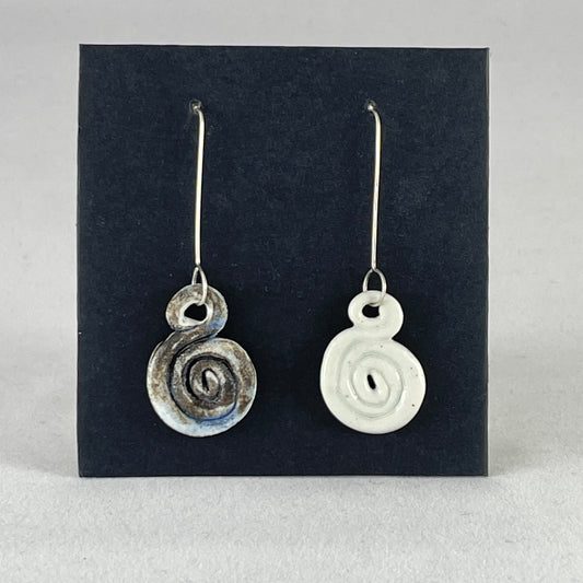 A pair of hand coiled porcelain earrings. One earring is white and the other is blue and black. Photographed on a black background. On sterling silver earrings hooks. 