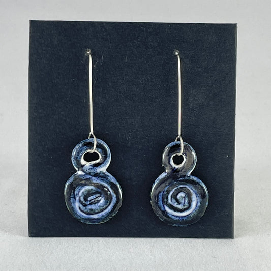 A pair of hand coiled porcelain earrings in dark blue. Photographed on a black background. On sterling silver earrings hooks.