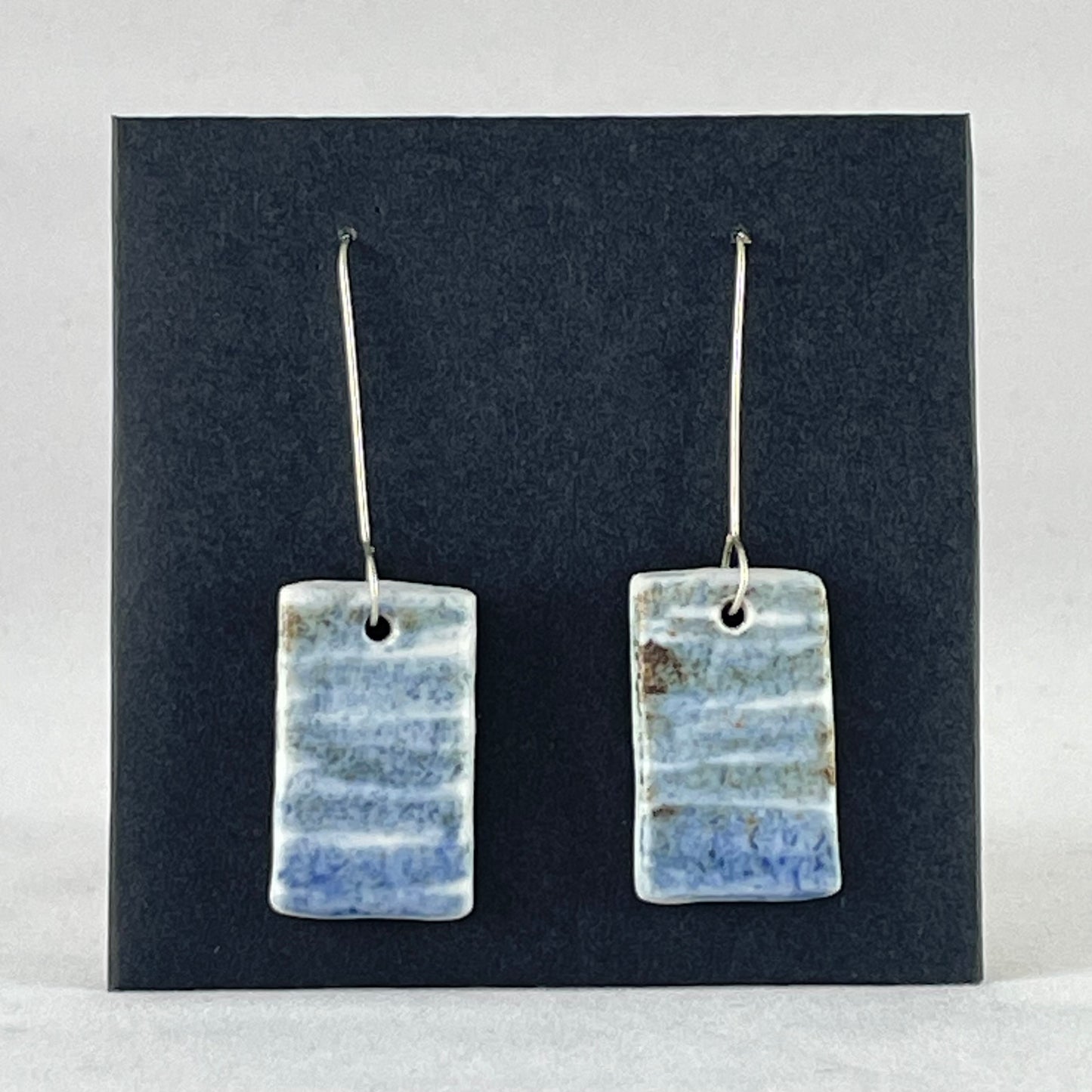 A pair of blue green and white porcelain earrings. Photographed on a black background. On sterling silver earrings hooks. 