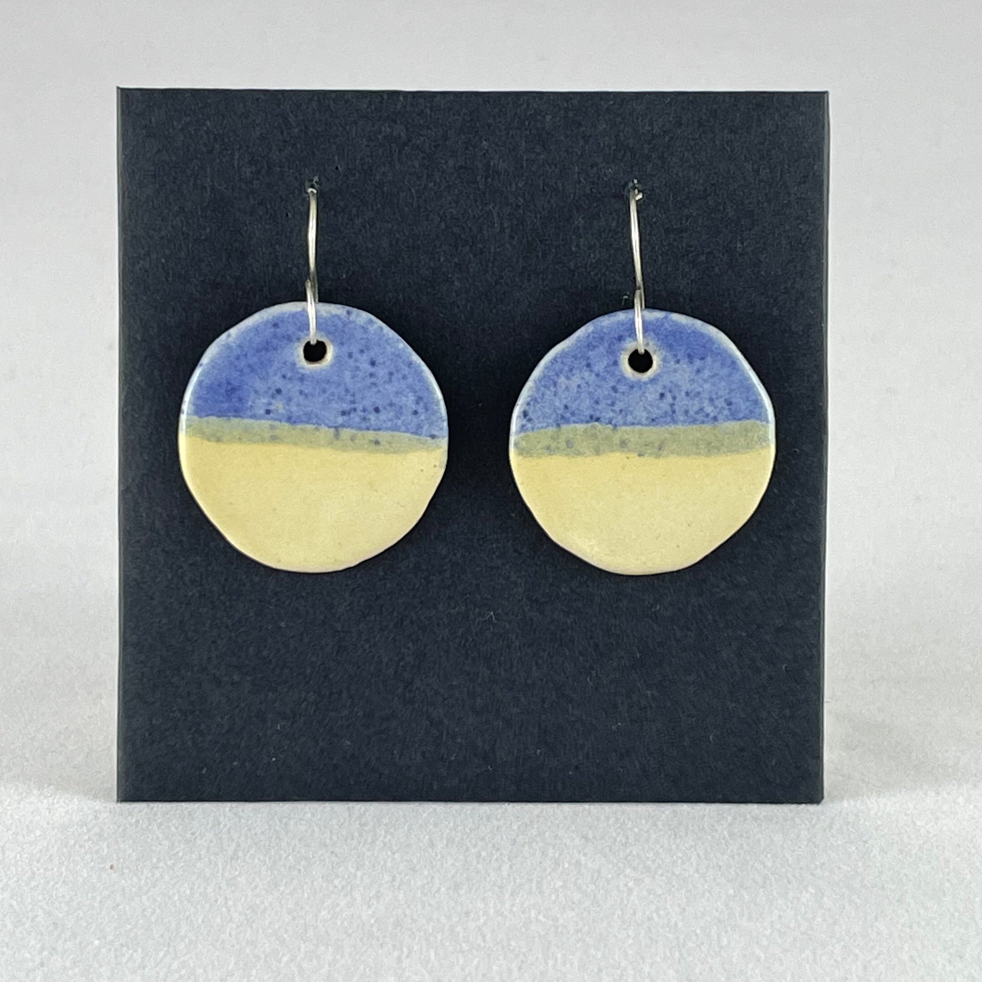 A pair of circular porcelain earrings in yellow and blue. On sterling silver earrings hooks. 