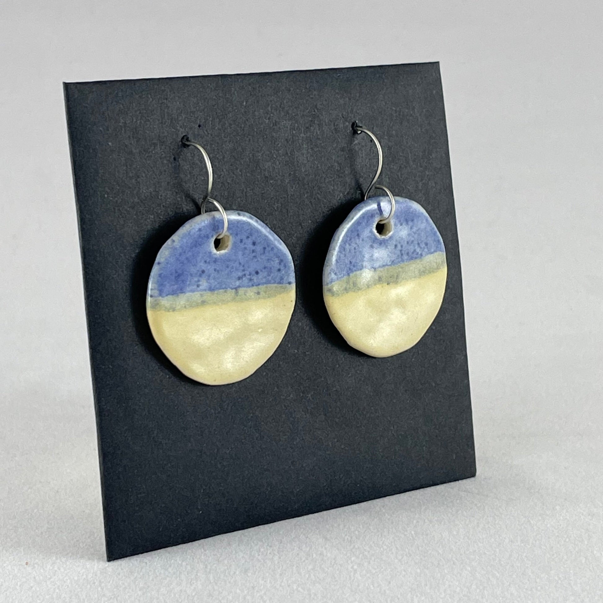 A pair of circular porcelain earrings in yellow and blue. On sterling silver earrings hooks. Side view
