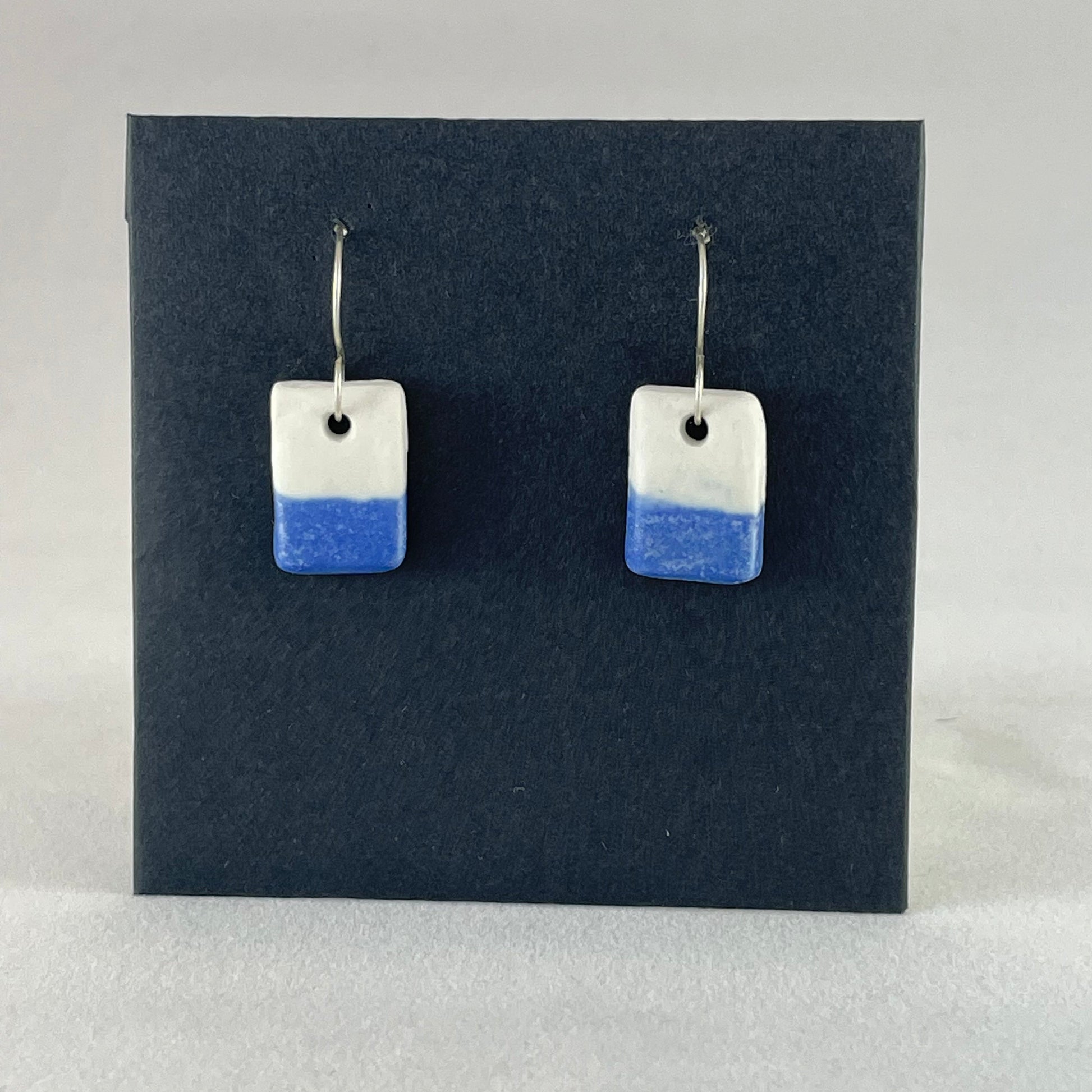 A pair of rectangular porcelain earrings in half white and half ultramarine blue. Photographed on a black background.