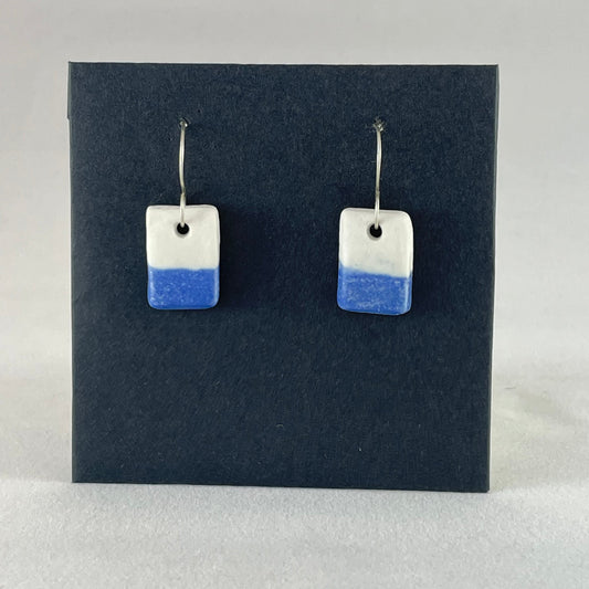A pair of rectangular porcelain earrings in half white and half ultramarine blue. Photographed on a black background.