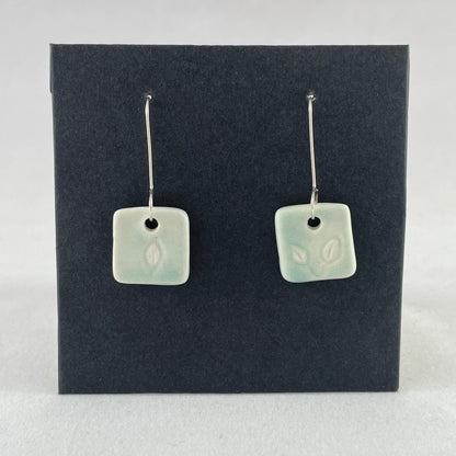 A pair of mint green square porcelain earrings on a black background. On sterling silver earrings hooks. 