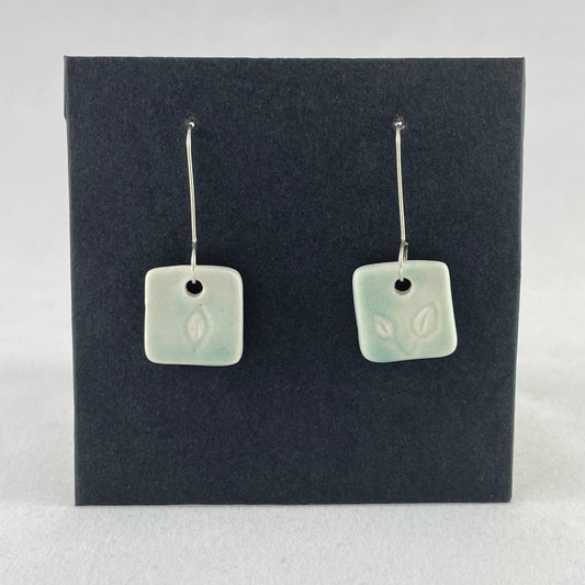 A pair of mint green square porcelain earrings on a black background. On sterling silver earrings hooks. 