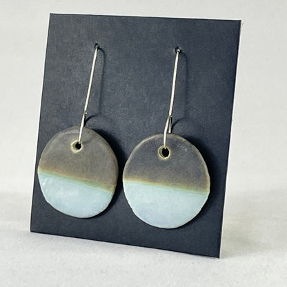 A pair of circular porcelain earrings in blue and green. On sterling silver earrings hooks. Side view