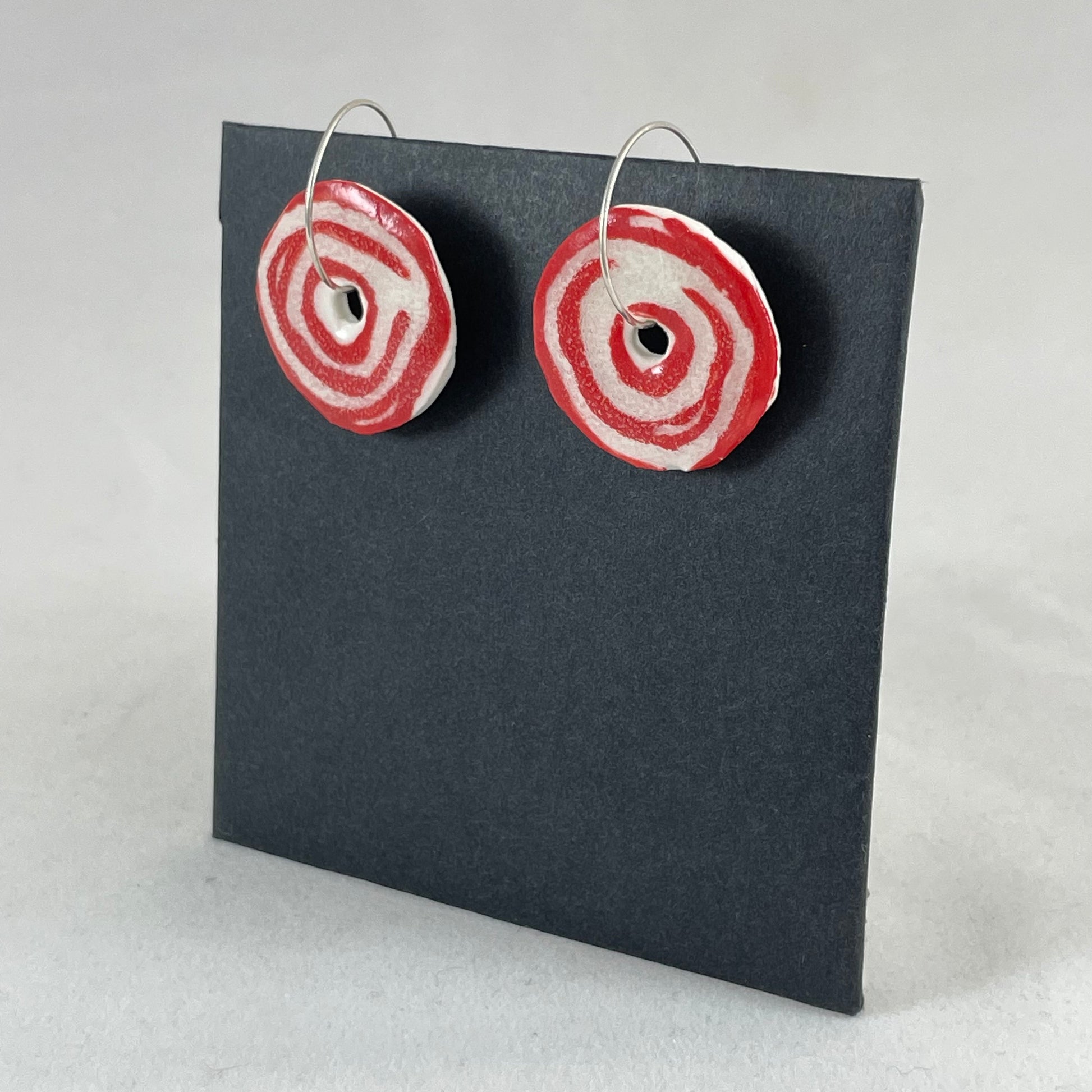A pair of red and white porcelain earrings on a black background. Simple rose pattern. Side view