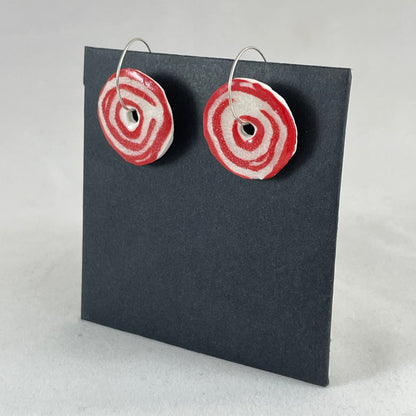 A pair of red and white porcelain earrings on a black background. Simple rose pattern. Side view