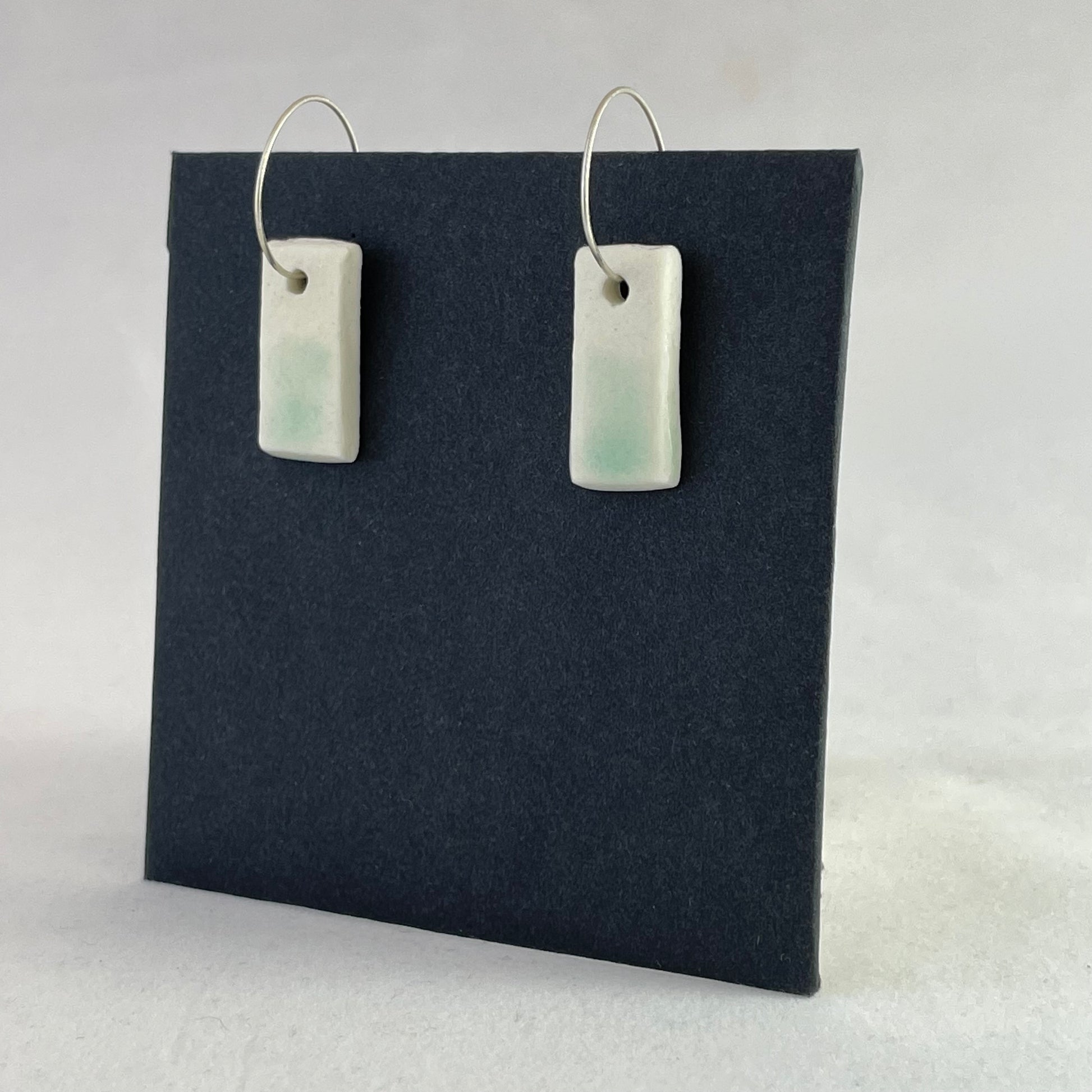 A pair of porcelain pendants in white with hint of green on a black background. Side view