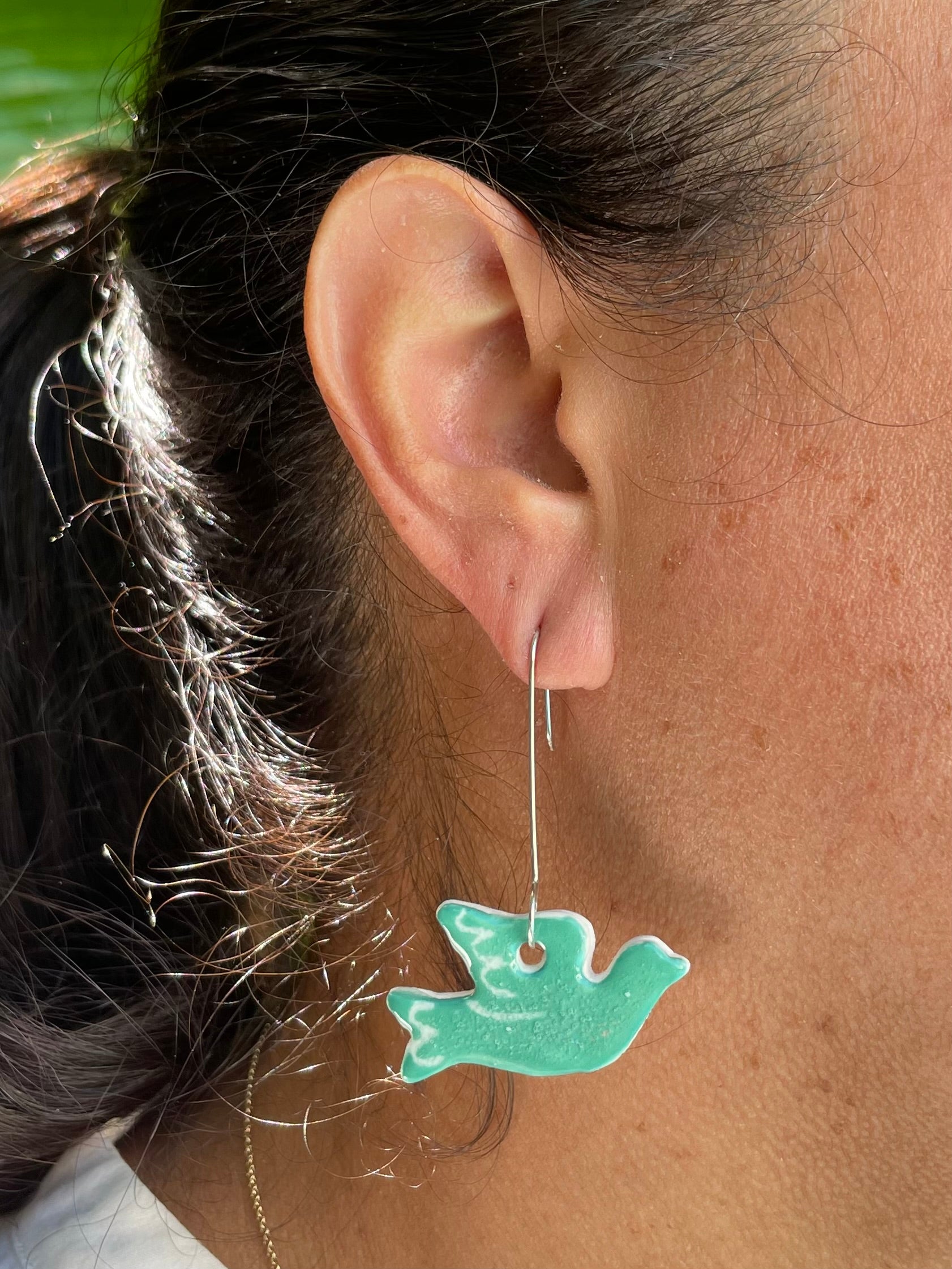 Closeup of woman wearing green dove earrings. Woman has olive skin and her dark brown hair is pulled back in ponytail