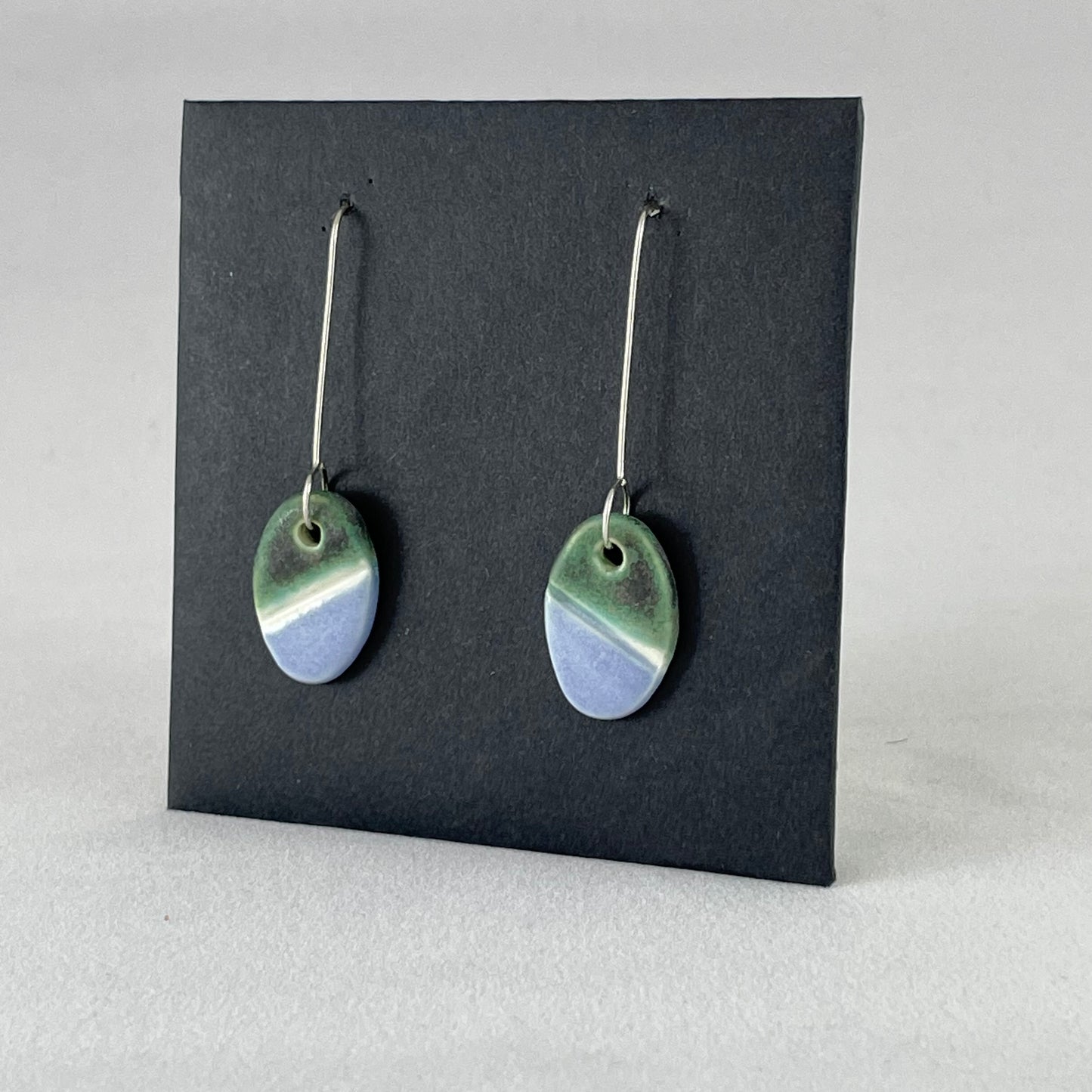 Side view of a pair of green, white and lilac-blue earrings on a black background. 