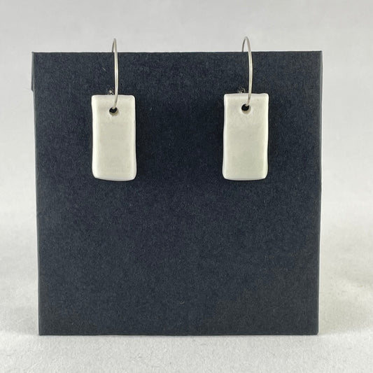 A pair of silver hoops with hand formed white porcelain pendants on a black background.