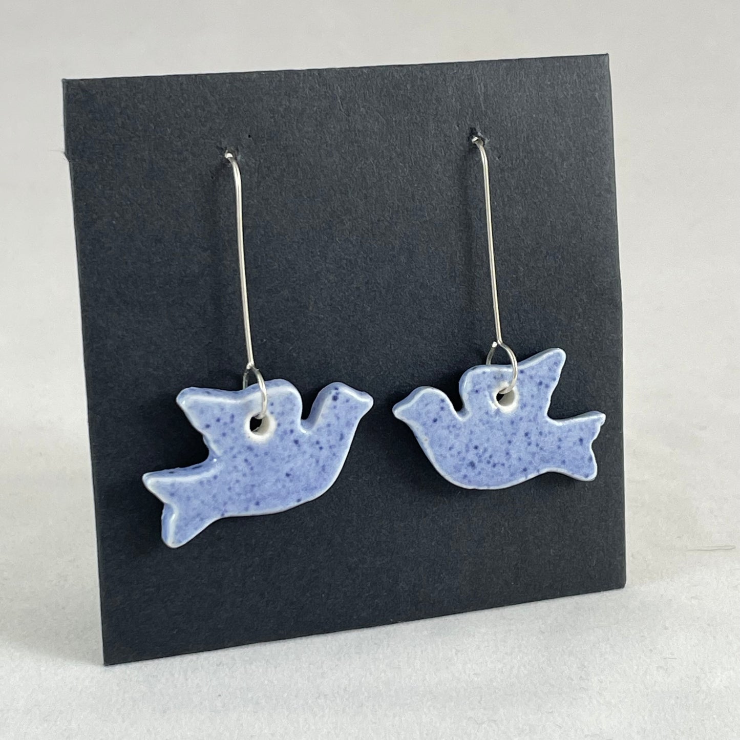 A pair of blue porcelain earrings in the shape of flying dove on a black background. Side view