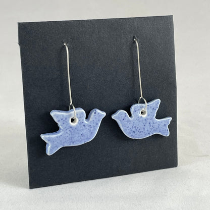 A pair of blue porcelain earrings in the shape of flying dove on a black background. Side view