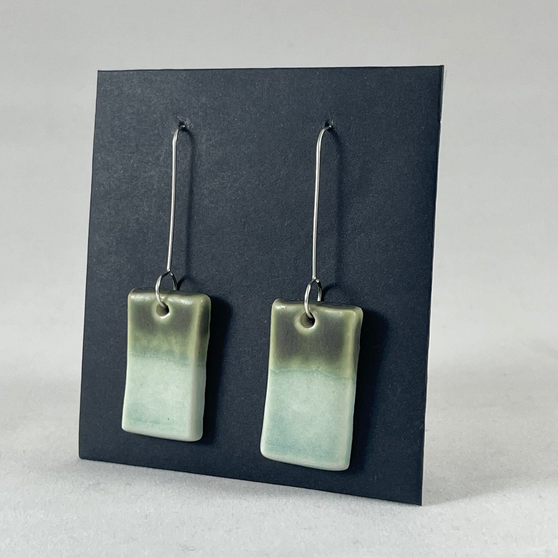 A pair of rectangular shaped porcelain earrings in mint and green. On sterling silver earrings hooks. Side view