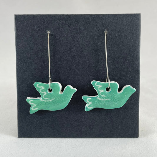 A pair of green porcelain earrings in the shape of flying dove on a black background.