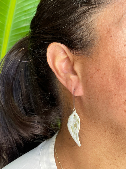 Closeup of woman wearing gum leaf earrings. Woman has olive skin and her dark brown hair is pulled back in ponytail. Sun is shining on her hair