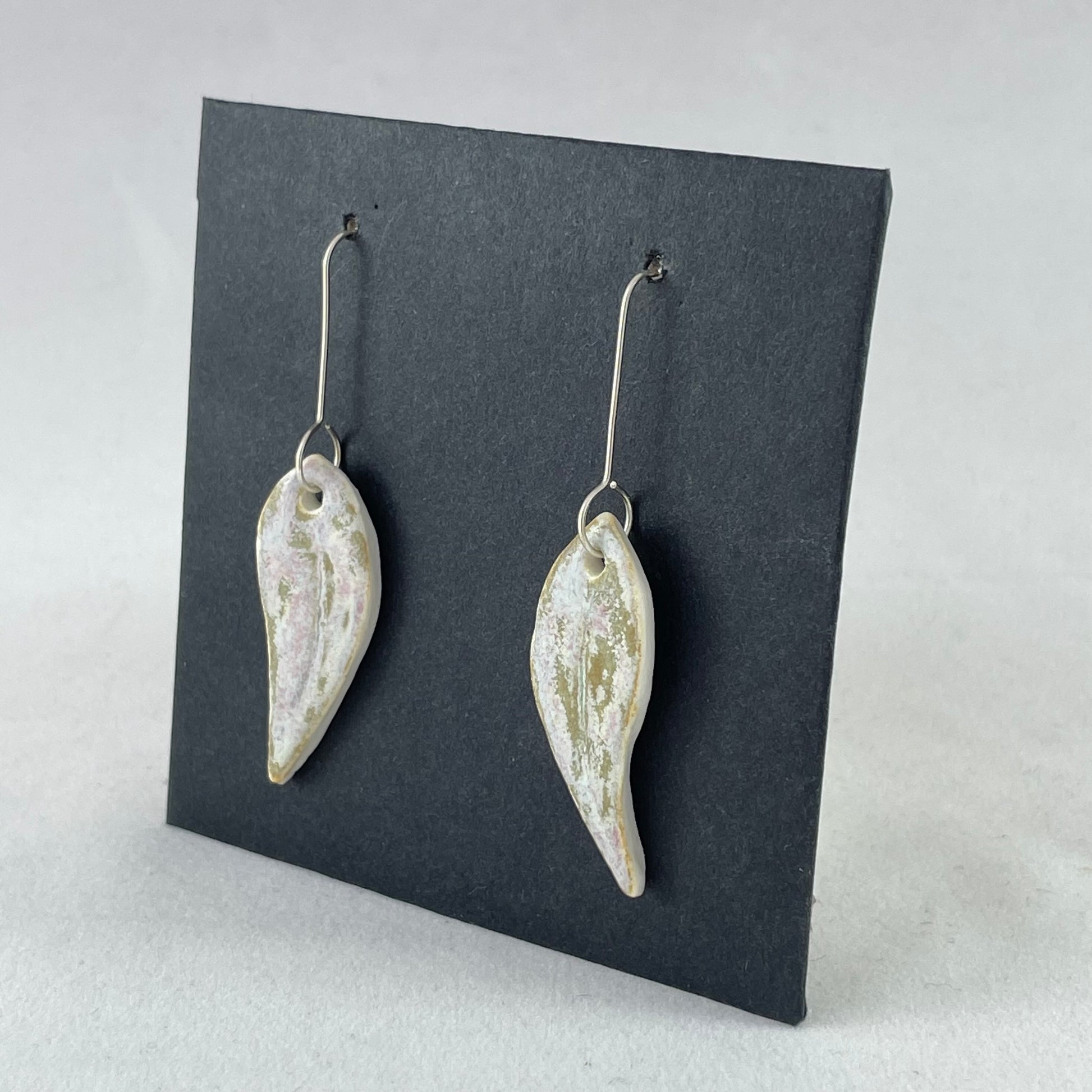 A pair of porcelain earrings in organic gum leaf shape. Photographed on a black background. Side view facing left