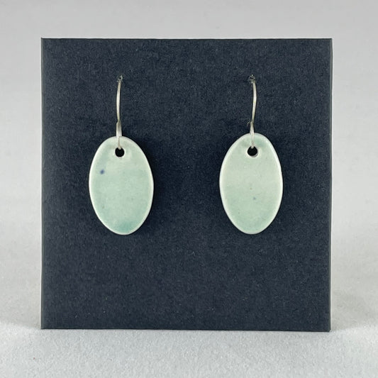 Pair of very pale mint green oval shaped porcelain earrings. Pictured in front of black background. 
