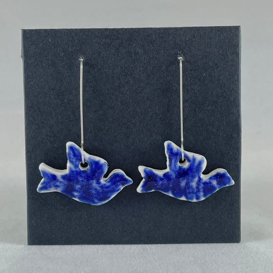 A pair of ultramarine blue porcelain earrings in the shape of flying dove on black card.