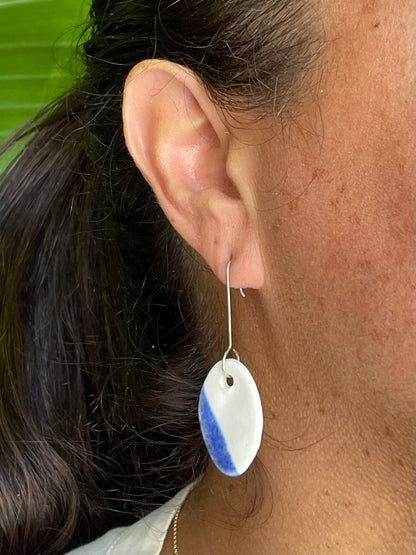 Closeup of woman wearing white and blue oval shaped earrings. Woman has olive skin and her dark brown hair is pulled back in ponytail.