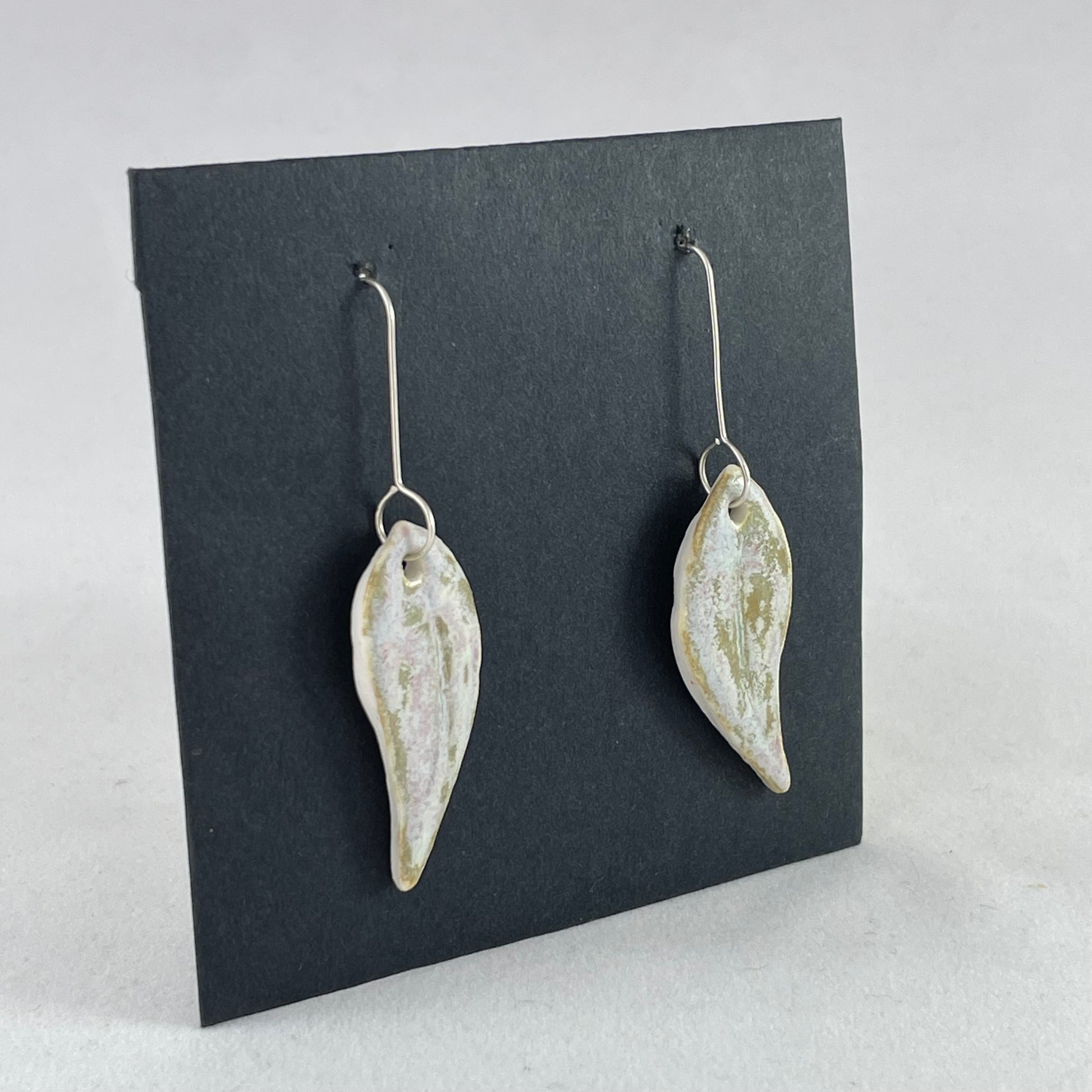 A pair of porcelain earrings in organic gum leaf shape. Photographed on a black background. Side view facing right 