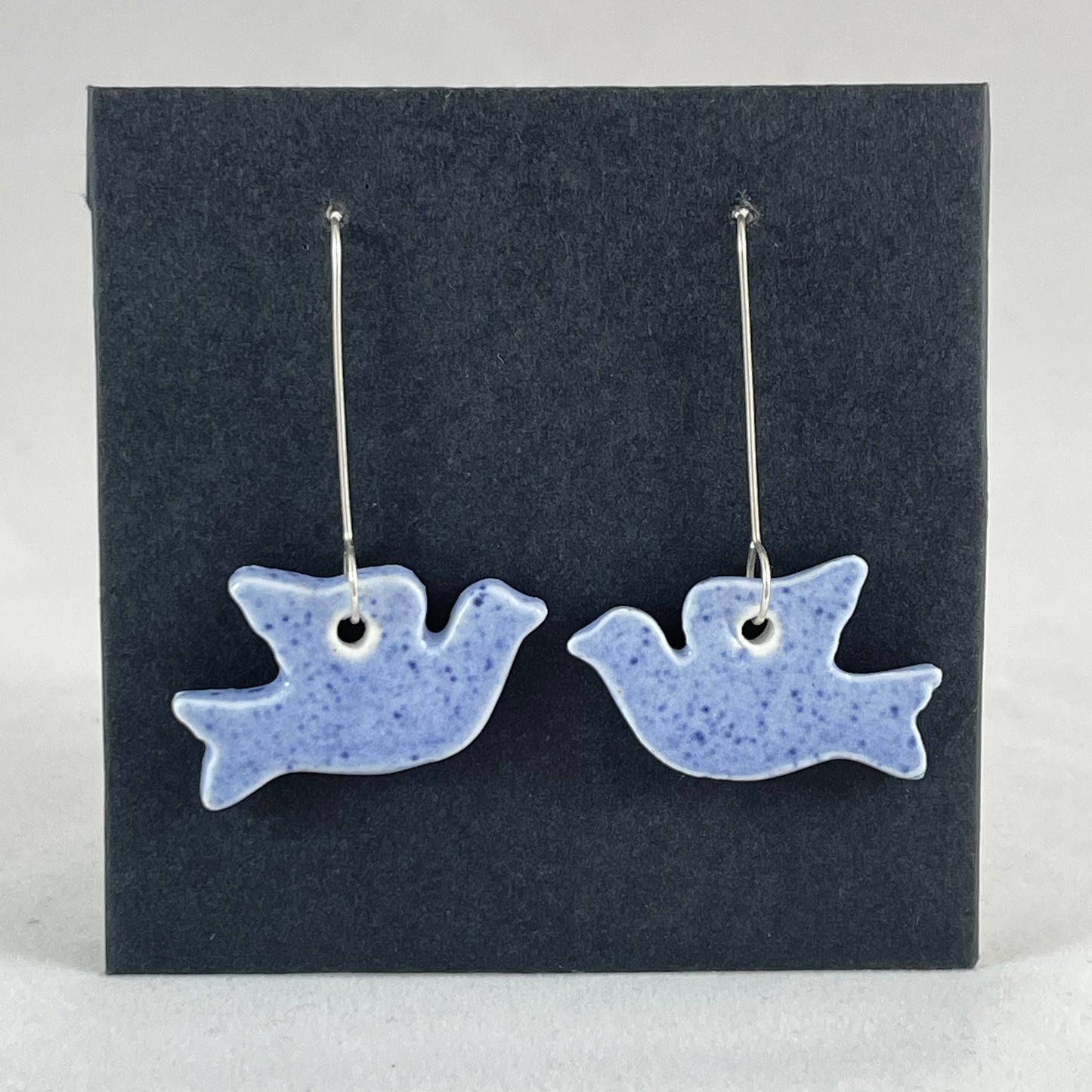 A pair of blue porcelain earrings in the shape of flying dove on a black background.