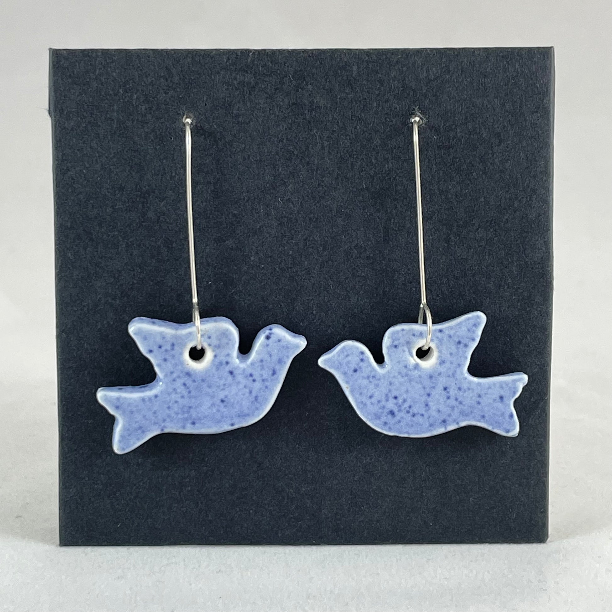 A pair of blue porcelain earrings in the shape of flying dove on a black background.