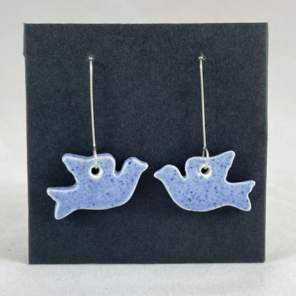 A pair of blue porcelain earrings in the shape of flying dove on a black background.