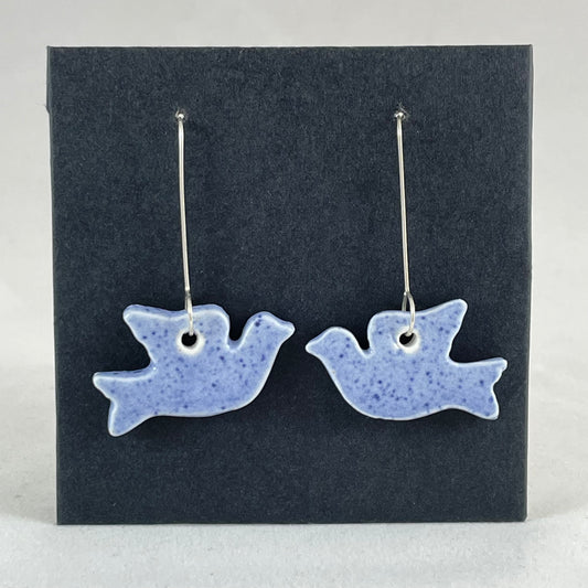 A pair of blue porcelain earrings in the shape of flying dove on a black background.