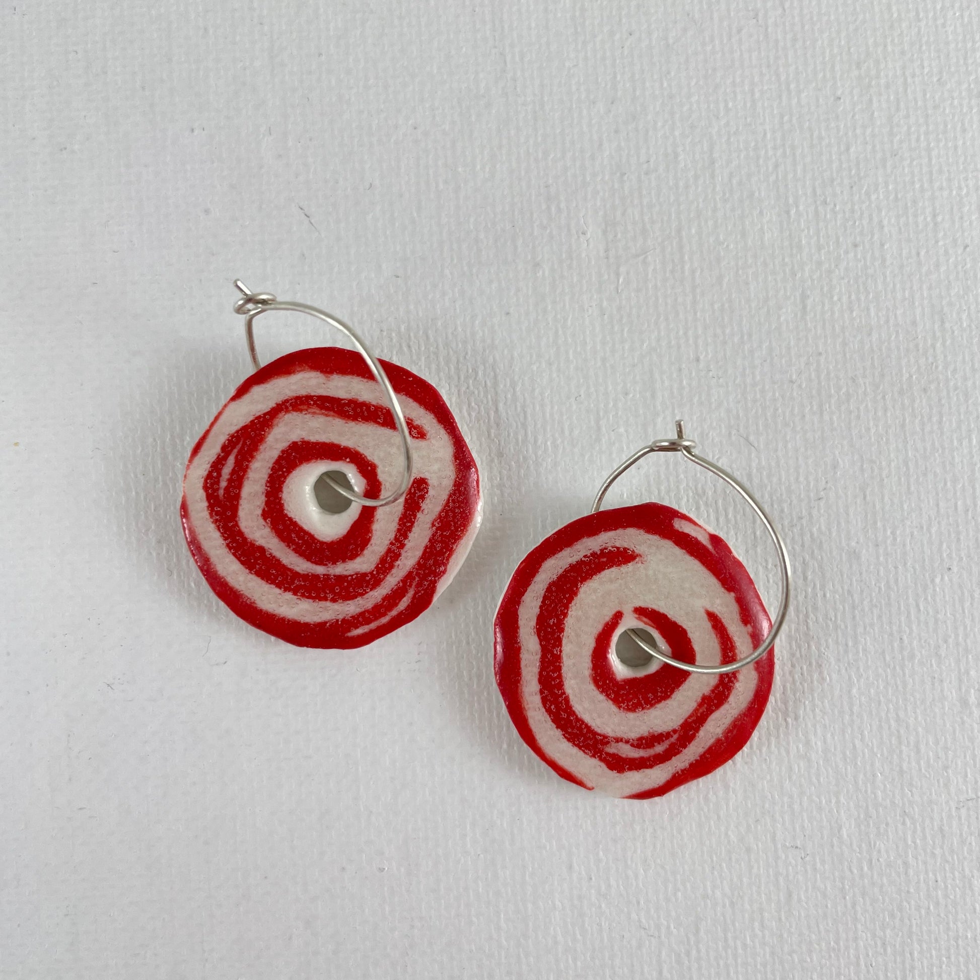 A pair of red and white porcelain earrings on a white background. Simple rose pattern.