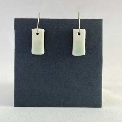 A pair of porcelain pendants in white with hint of green on a black background.