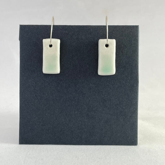 A pair of porcelain pendants in white with hint of green on a black background.