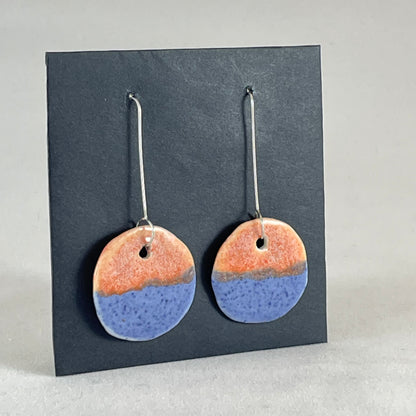 A pair of circular shaped porcelain earrings in blue and orange. On sterling silver earrings hooks. Side view