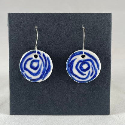 A pair of blue and white porcelain earrings hanging on black card. Simple rose pattern with loosely painted blue circles on white porcelain.