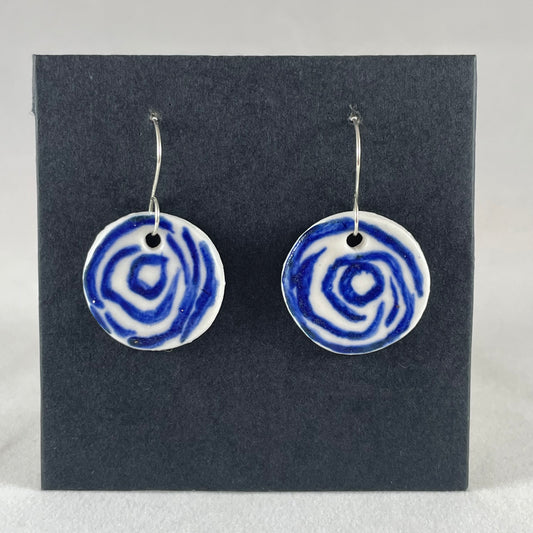 A pair of blue and white porcelain earrings hanging on black card. Simple rose pattern with loosely painted blue circles on white porcelain.