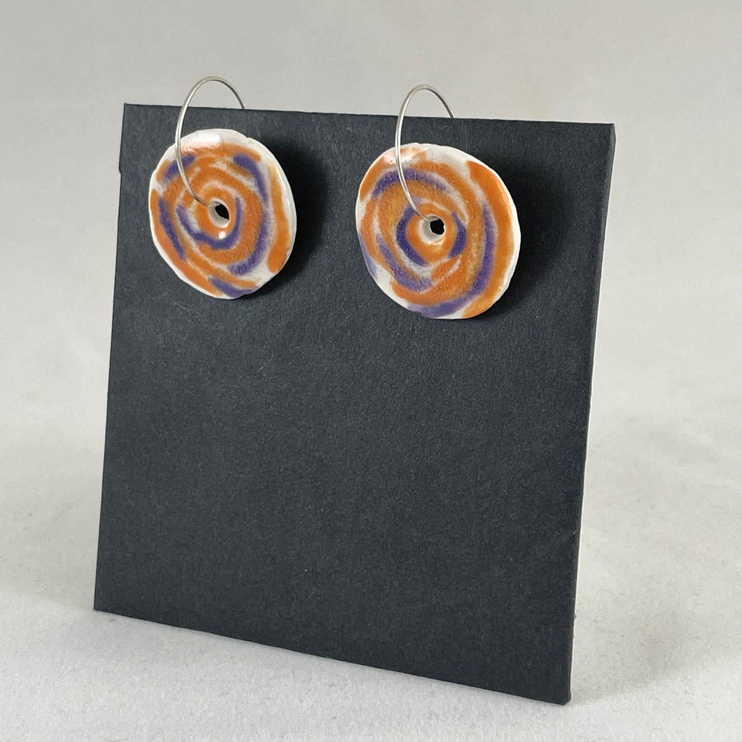 A pair of lavender and orange porcelain earrings on a black background. Simple rose pattern. Side view