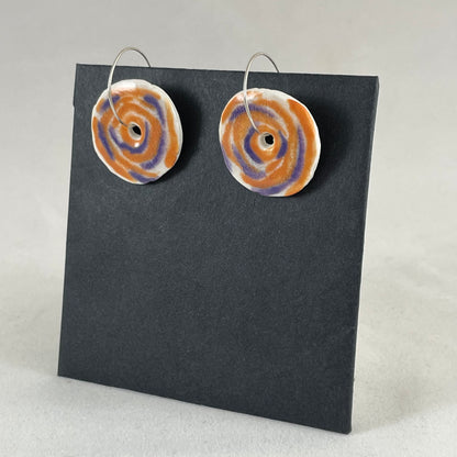 A pair of lavender and orange porcelain earrings on a black background. Simple rose pattern. Side view